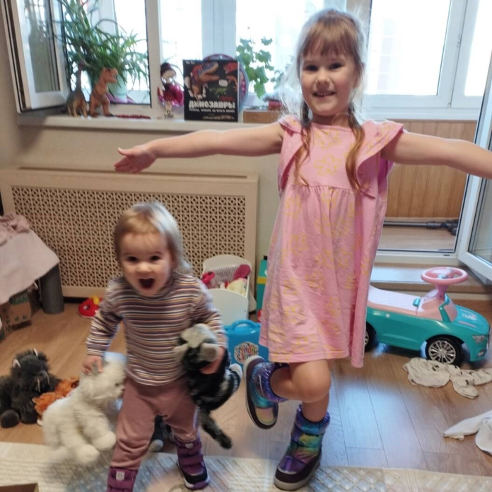 Две радующиеся девочки на фоне игрушек. Обстановка - квартира.