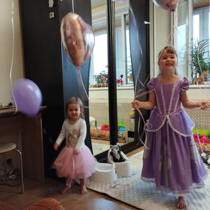 День рождения. Две радостные девочки в нарядных платьях с шариками в руках. 
                Обстановка - квартира.