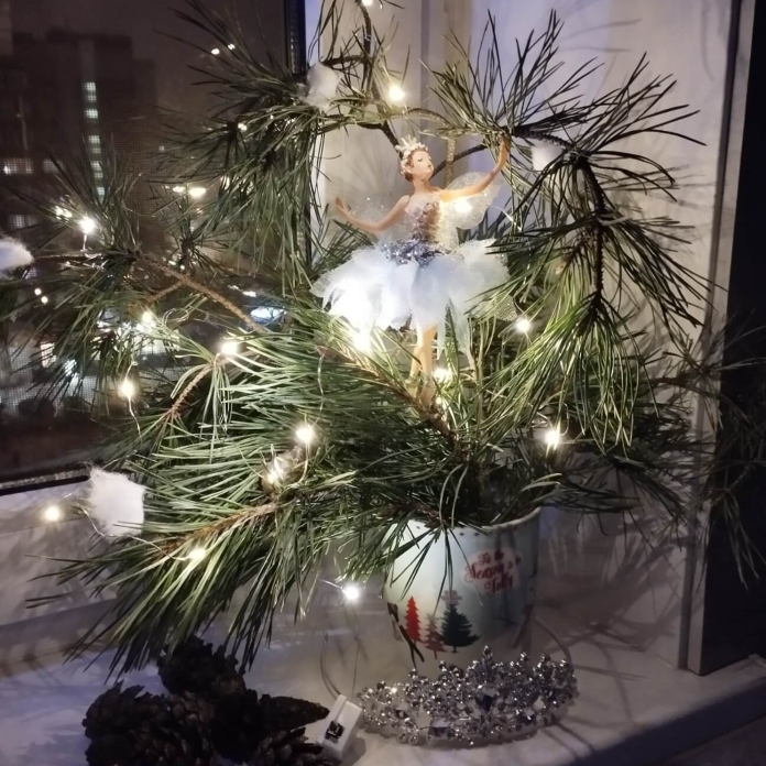 Ночь на кухне. На подоконнике в новогодней кружке стоят веточки сосны, украшенные 
                гирляндой и ёлочной игрушкой - балерина в голубом платье.